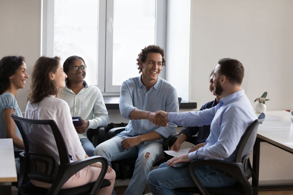 Two men shaking hands in Clarity Psychology group session with participants seated in a circle.