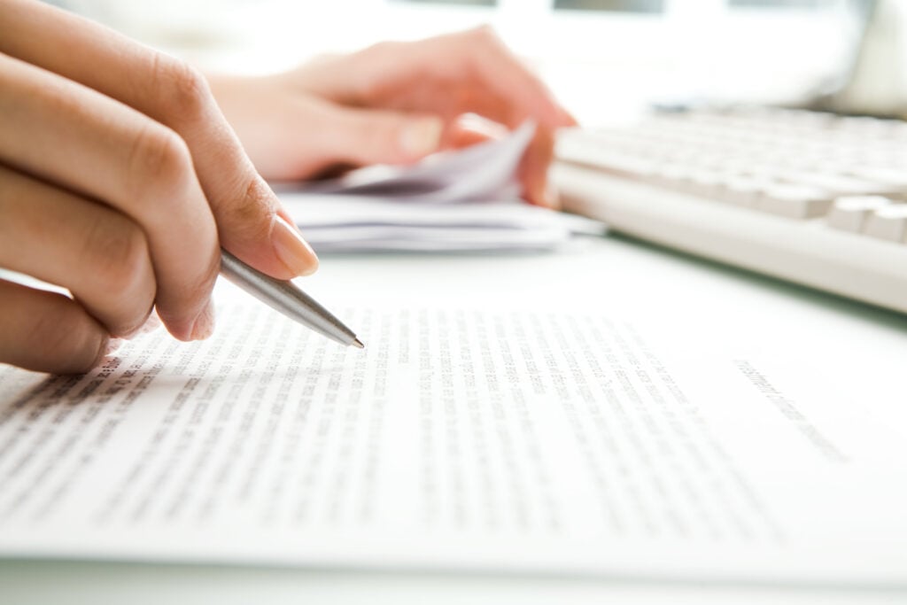 Close-up of hand editing printed paperwork at Clarity Psychology with keyboard and documents in background